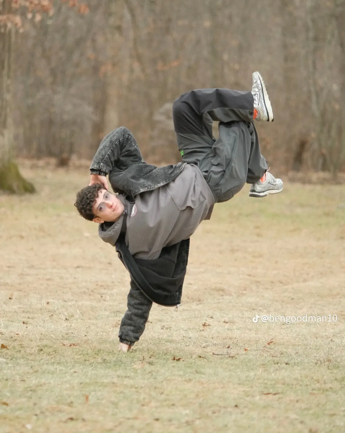 Ben Goodman holding a one-handed breaking freeze outdoors, legs extended above him